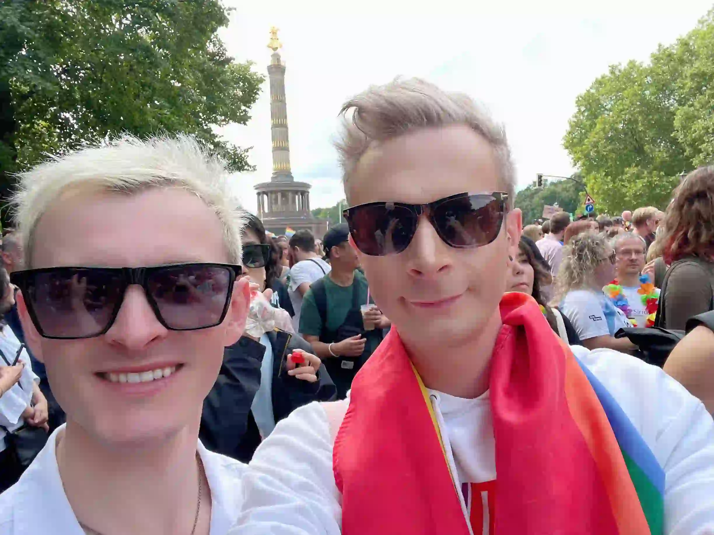 Joe and Alex standing at Berlin Pride in front of the Victory Column during the parade.